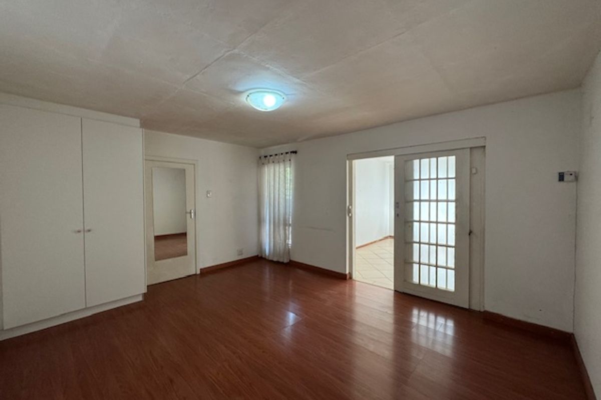 An empty bedroom featuring laminate flooring, a built-in wardrobe, and a glass-paneled door leading to an adjacent space.