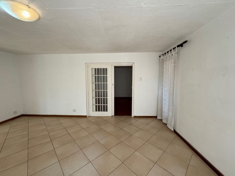 An empty living room featuring neutral ceramic floor tiles, a sliding glass panel door, and simple ceiling lighting, offering a blank canvas for interior design.