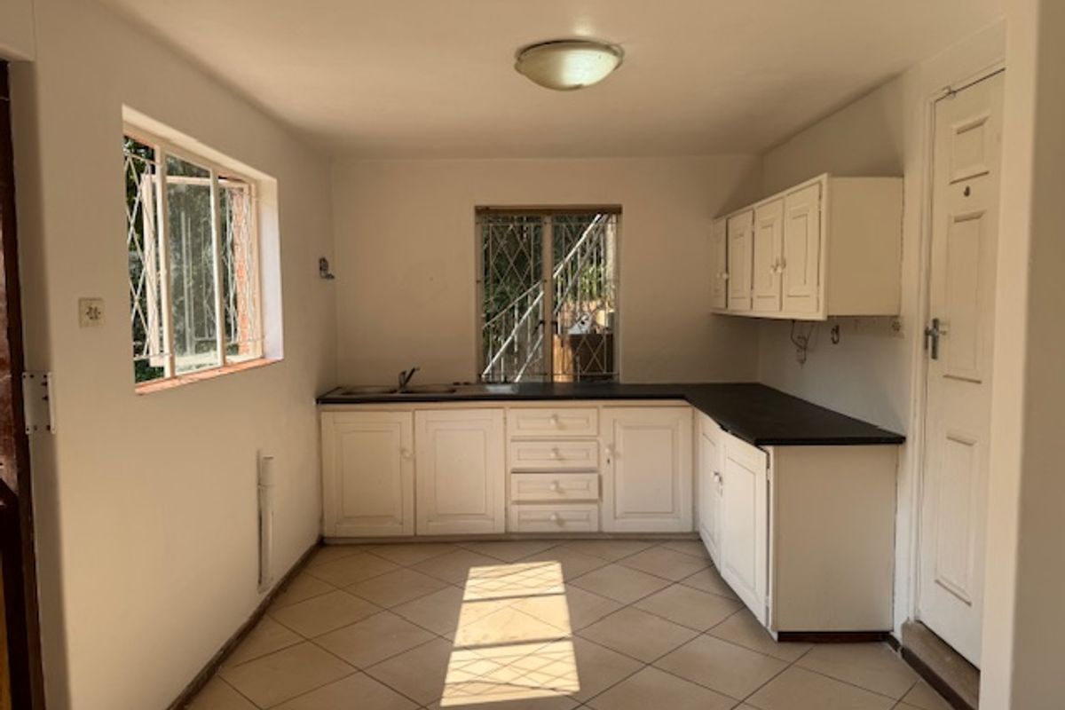 A functional, empty kitchen featuring white built-in cabinetry, dark laminate countertops, tiled flooring, and security bars on the windows.