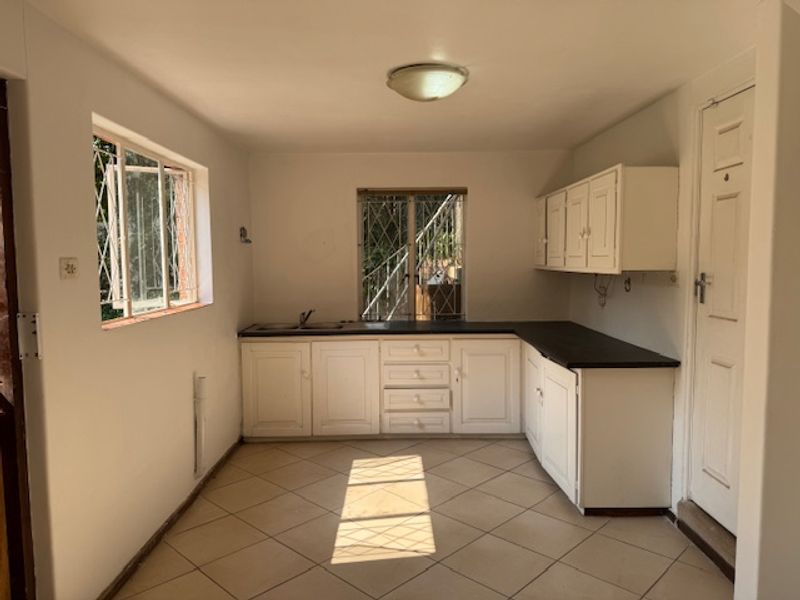 A functional, empty kitchen featuring white built-in cabinetry, dark laminate countertops, tiled flooring, and security bars on the windows.