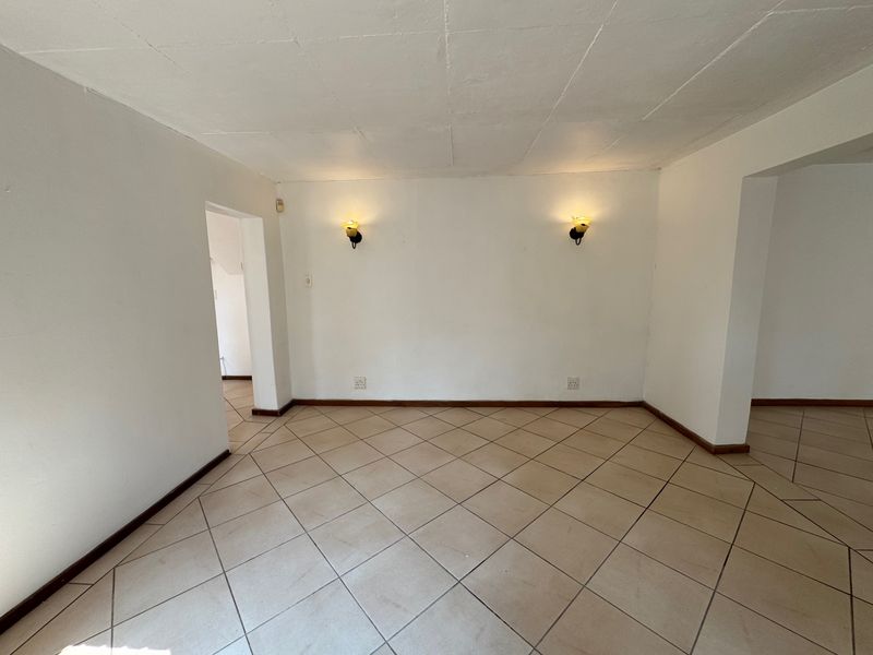 An empty living area featuring neutral tiled flooring and wall-mounted lighting, offering a blank canvas for interior design and personalization.