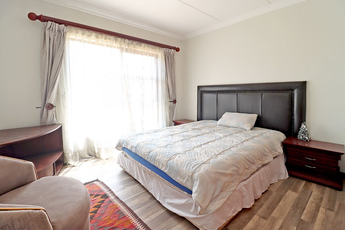 A well-lit bedroom featuring wood-look flooring, crown molding, and a large window with curtain rod.