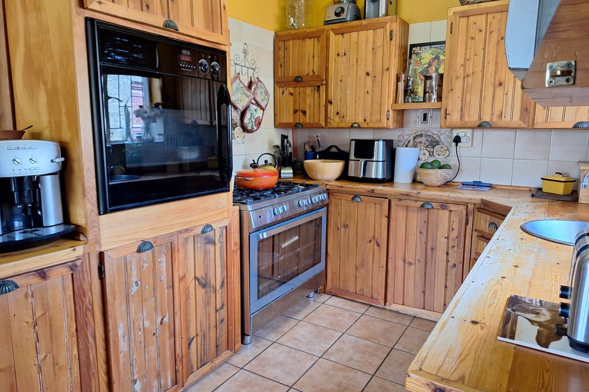 A functional kitchen featuring rustic wooden cabinetry, a built-in oven, gas hob, and tiled flooring, offering a traditional aesthetic with potential for modernization.