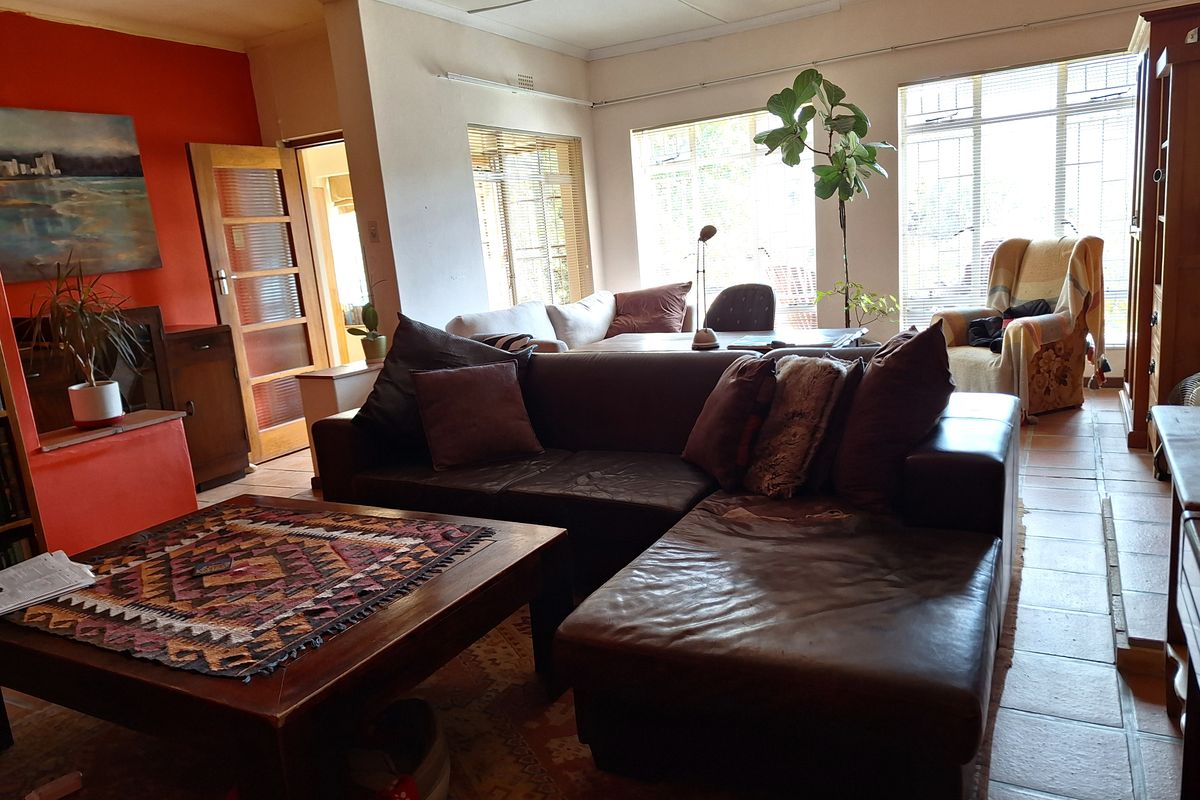 Spacious living room featuring tiled flooring, large windows with security bars, and an open-plan layout with access to adjacent rooms.