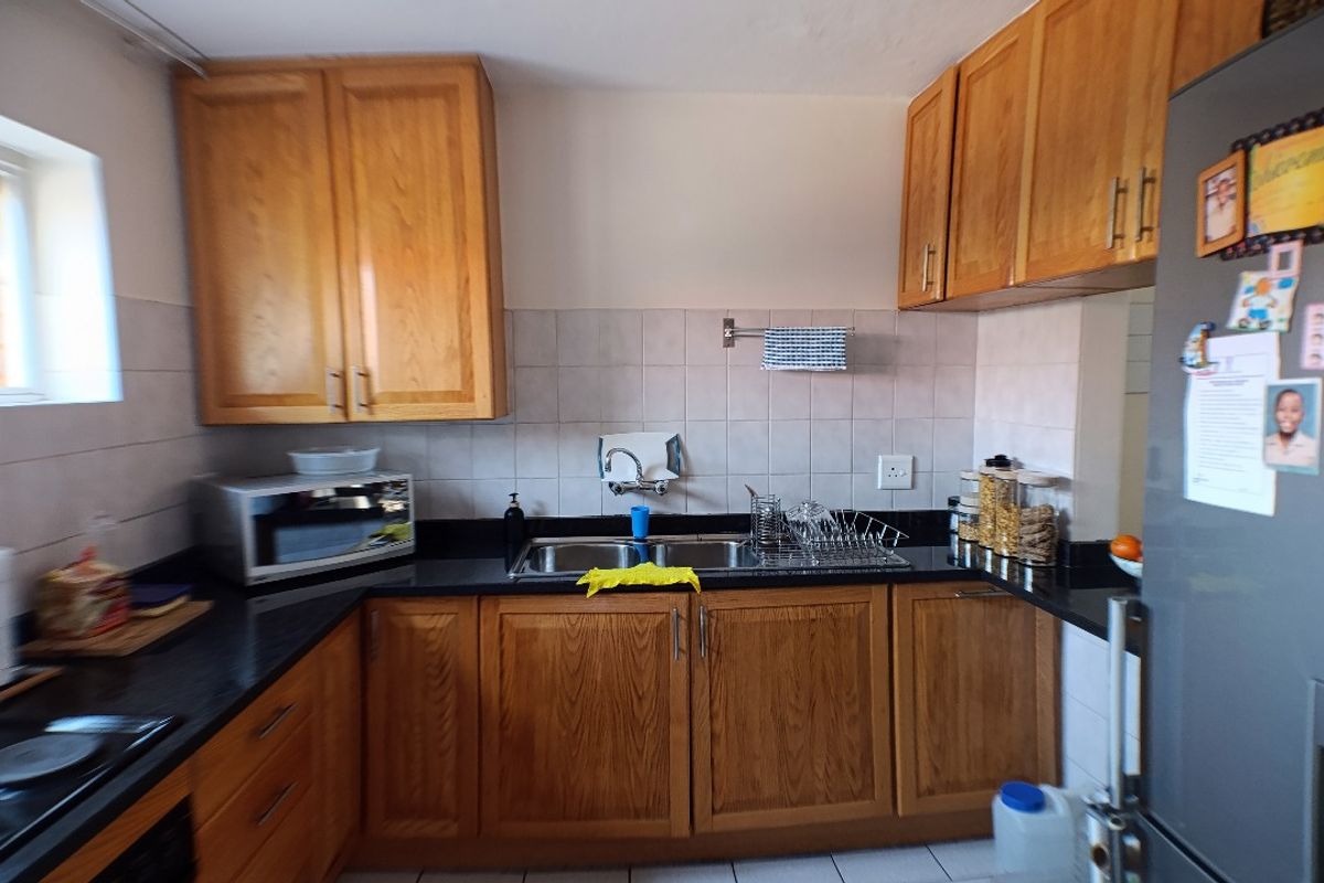 A functional kitchen featuring wooden cabinetry, black granite countertops, a double basin sink, and a tiled backsplash.