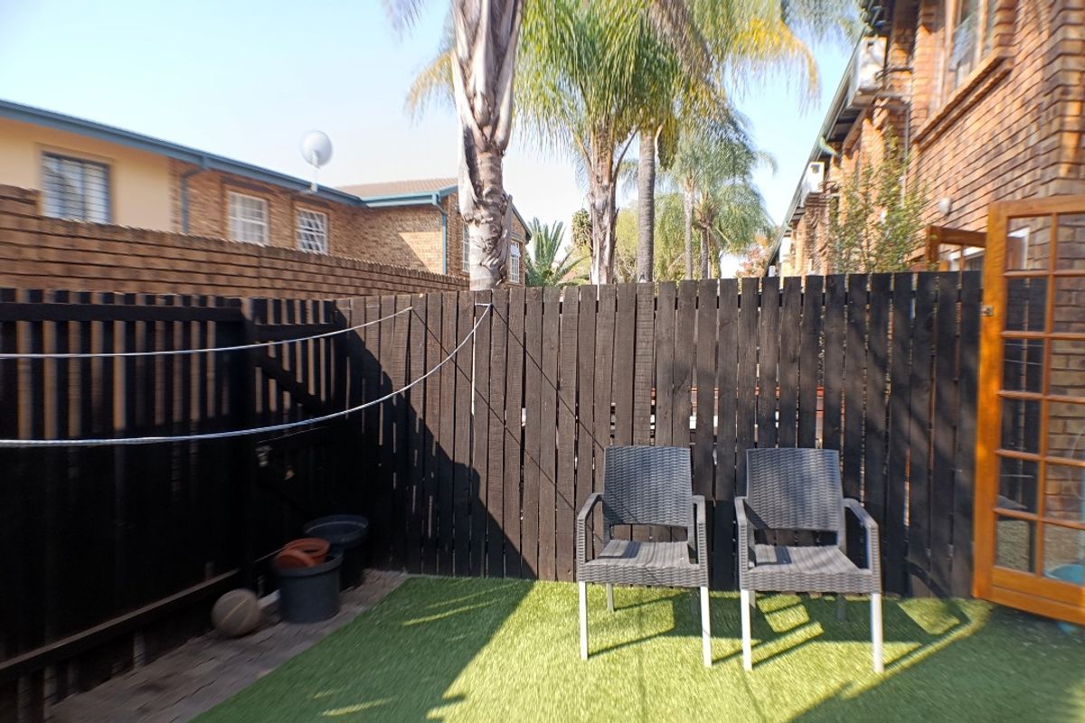 A private rear courtyard featuring artificial turf, a dark timber privacy fence, and direct access to the apartment through a timber-framed glass door.