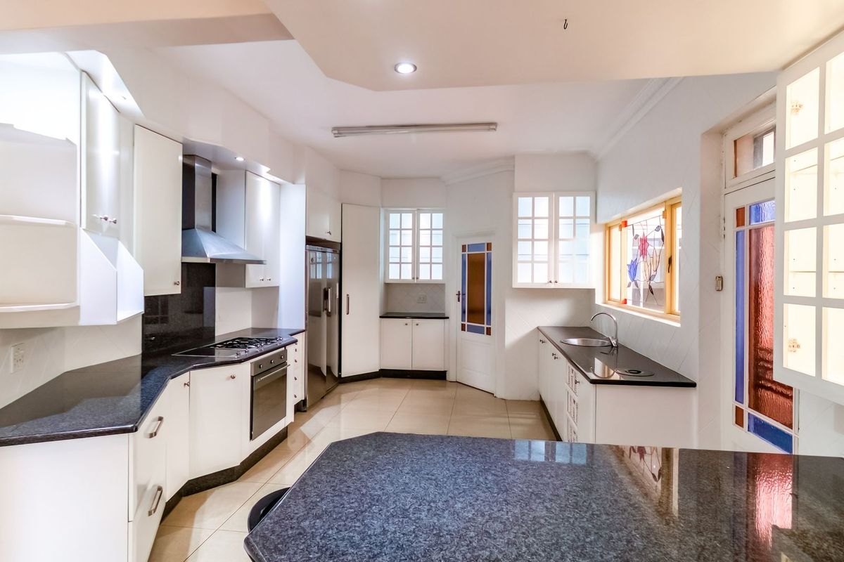A spacious, well-lit kitchen featuring granite countertops, built-in cabinetry, a gas hob with extractor, and a unique stained glass window detail.
