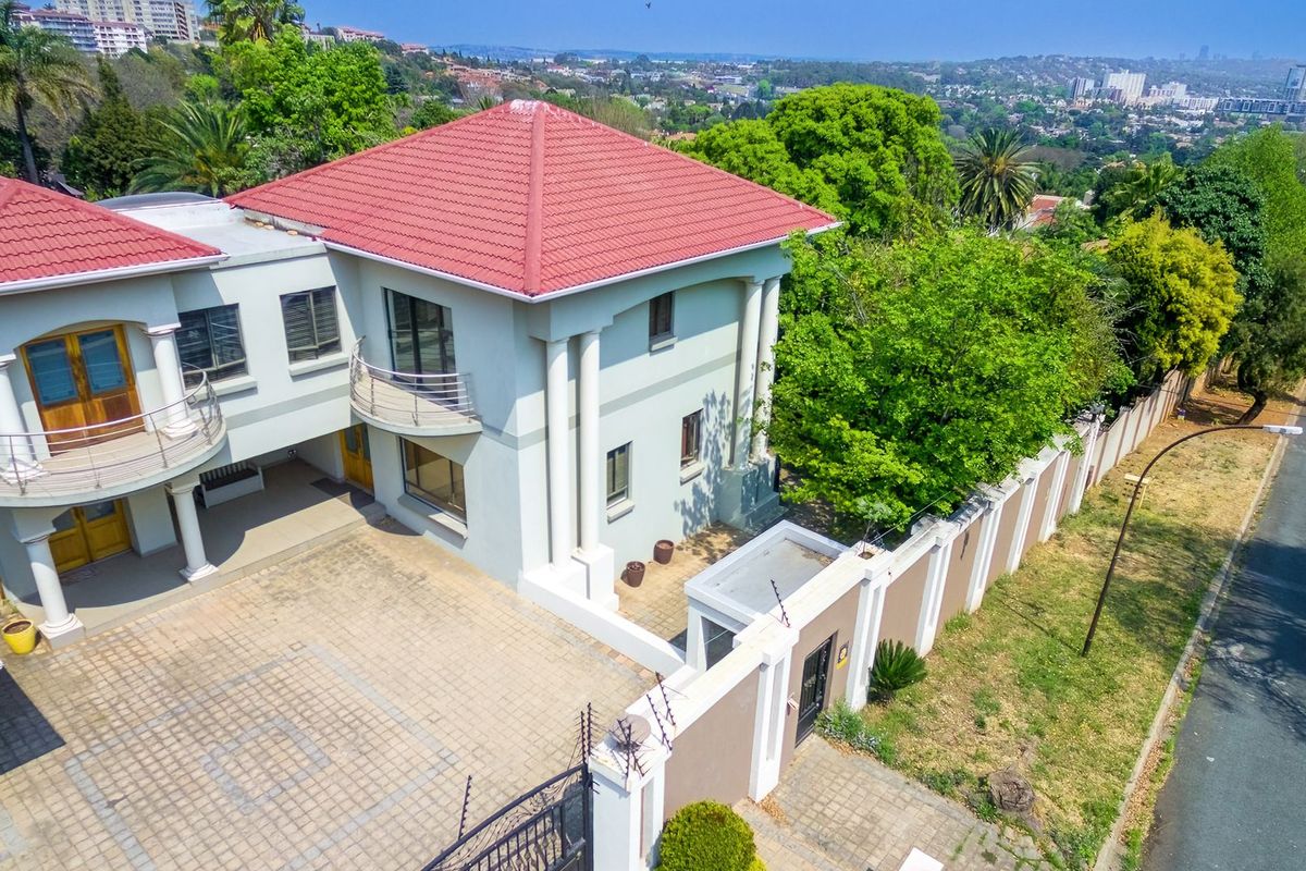 Aerial view of a double-story residential property featuring a tiled roof, paved driveway, perimeter wall with electric fencing, and elevated balconies.