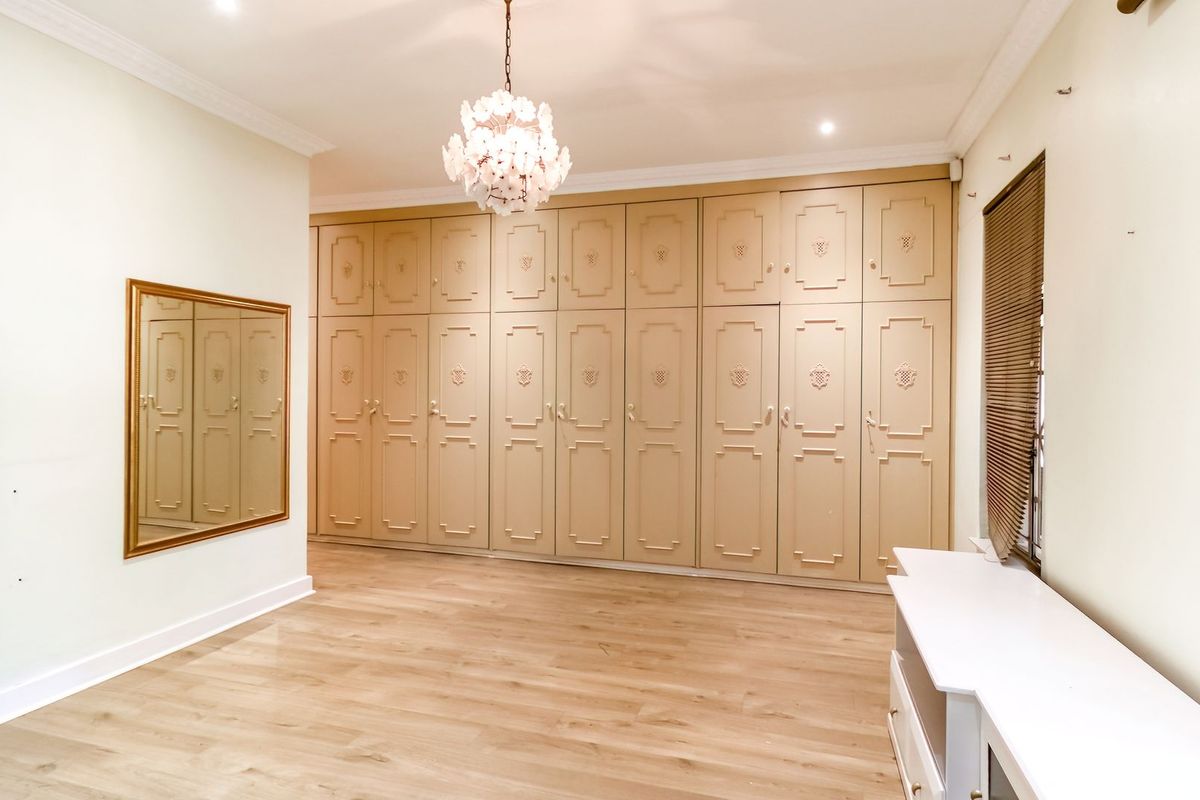 Spacious bedroom featuring extensive floor-to-ceiling built-in cabinetry, crown molding, and light wood-look flooring, offering a clean and versatile living space.