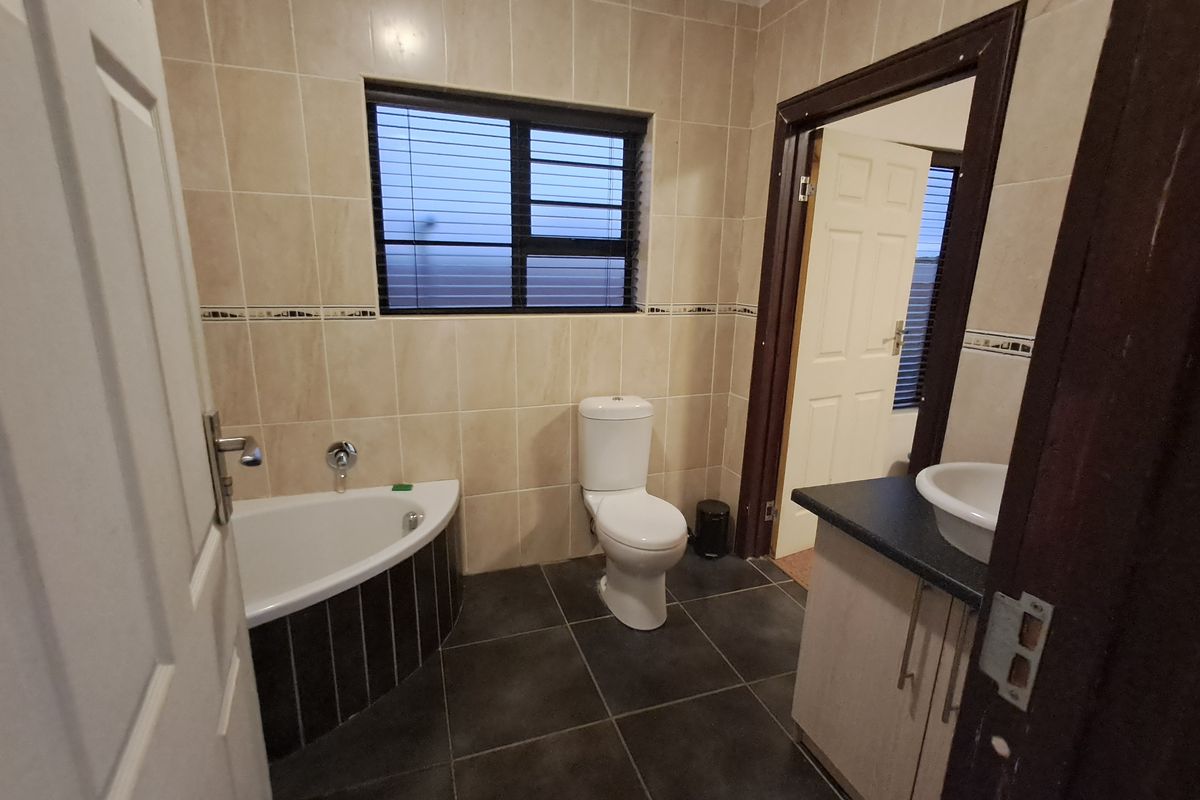 A functional bathroom featuring a corner bathtub, a vanity with a vessel sink, and neutral wall tiling with dark floor tiles.