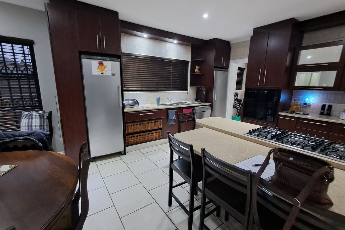 Spacious kitchen featuring dark wood cabinetry, stone countertops, a central island with a gas cooktop, and tiled flooring.