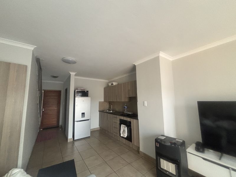 Open plan living area featuring a compact kitchen with built-in cabinetry, oven, hob, and tiled flooring throughout.