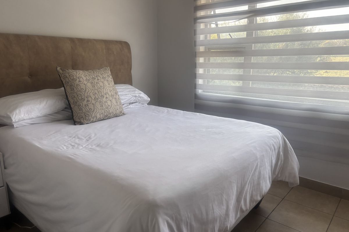 A well-lit bedroom featuring neutral tiled flooring and modern dual-layer roller blinds, providing a clean and functional living space.