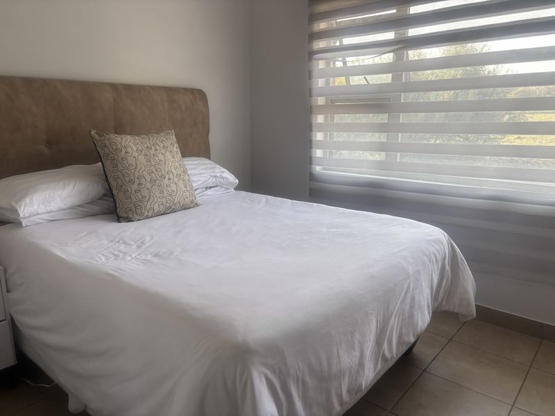 A well-lit bedroom featuring neutral tiled flooring and modern dual-layer roller blinds, providing a clean and functional living space.