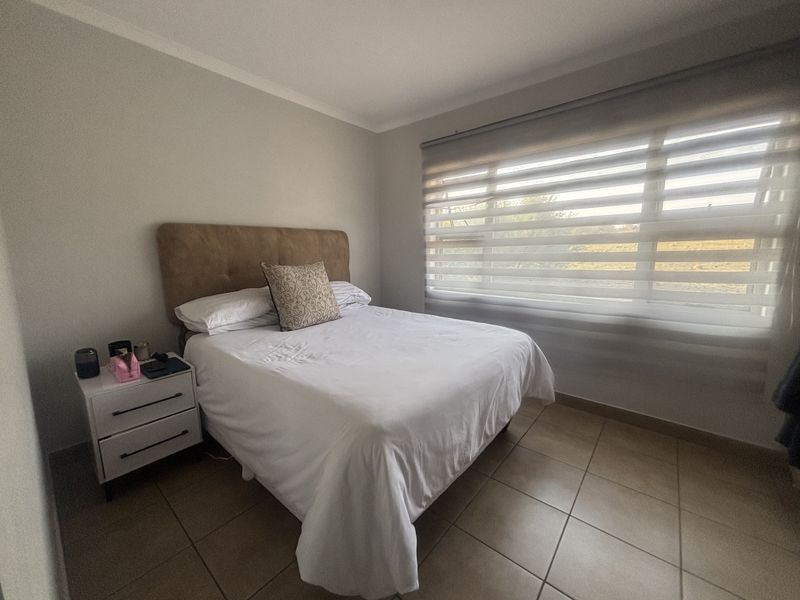A well-lit bedroom featuring neutral wall tones, tiled flooring, and modern zebra blinds, providing a comfortable and functional living space.