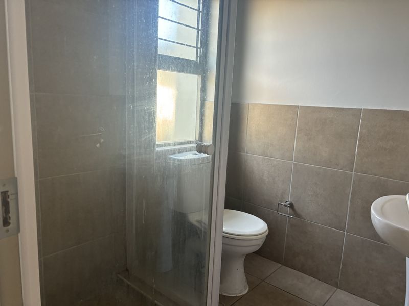 A functional bathroom featuring a shower enclosure, toilet, and pedestal basin with neutral wall and floor tiling.