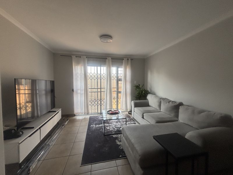 A living room featuring tiled flooring and a sliding door with a security gate, providing access to the exterior.