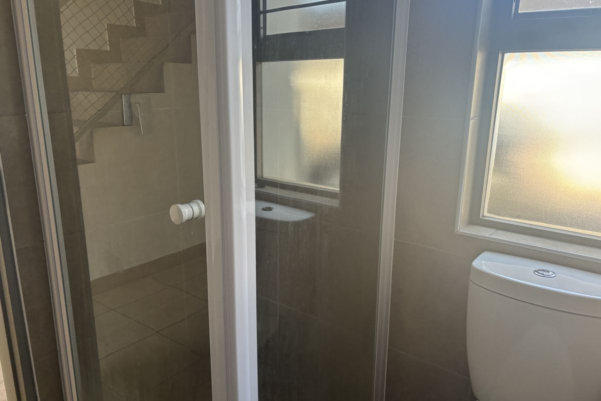 A functional bathroom featuring a toilet, shower enclosure with glass door, and tiled finishes, illuminated by natural light through a frosted window.