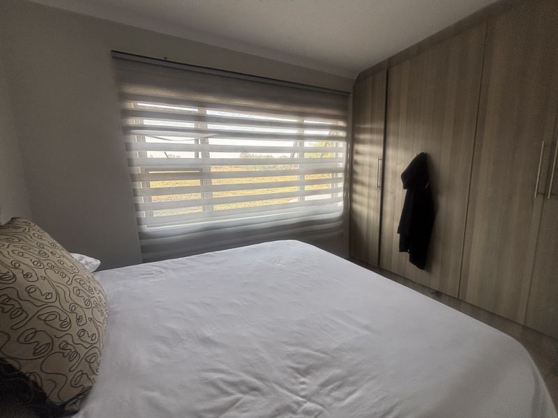 A well-maintained bedroom featuring built-in wooden cupboards and modern roller blinds, offering a clean and functional living space.