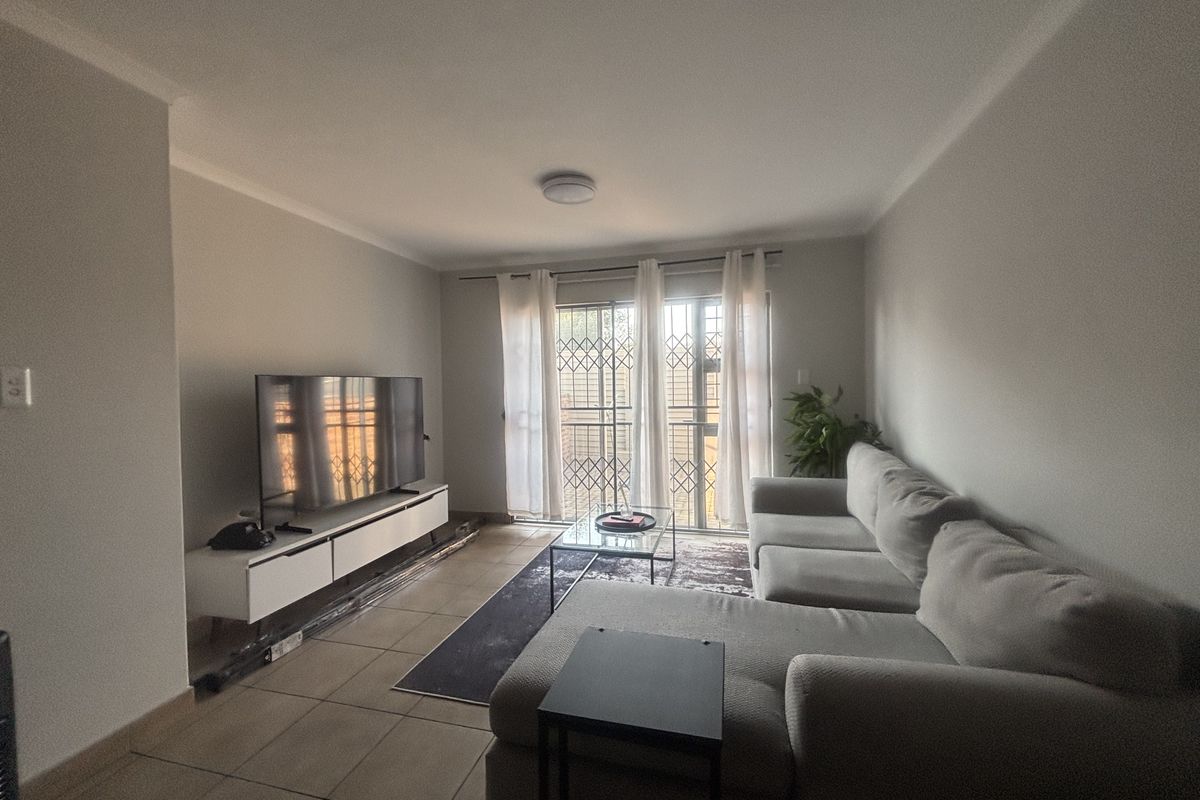 A living room featuring tiled flooring, a sliding glass door with a security gate, and neutral wall finishes.