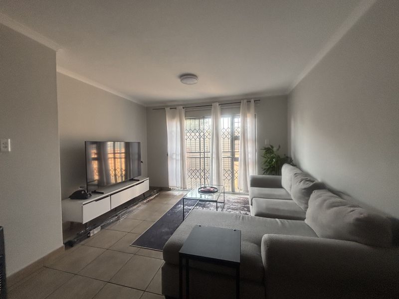 A living room featuring tiled flooring, a sliding glass door with a security gate, and neutral wall finishes.