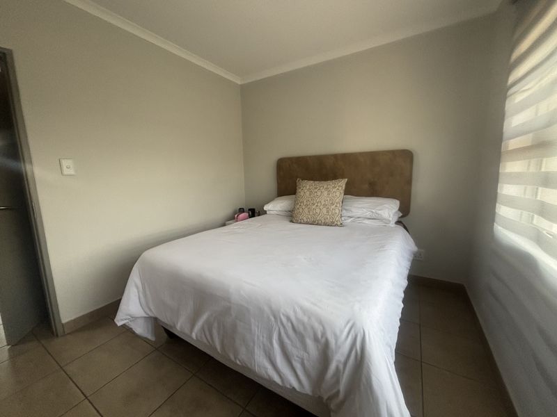 A compact bedroom featuring neutral wall tones, tiled flooring, and modern roller blinds, providing a functional and clean living space.
