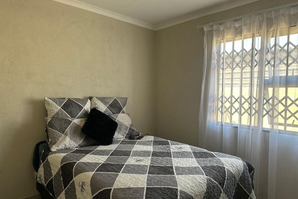 A standard bedroom featuring neutral wall tones, tiled flooring, and a window fitted with a security gate.