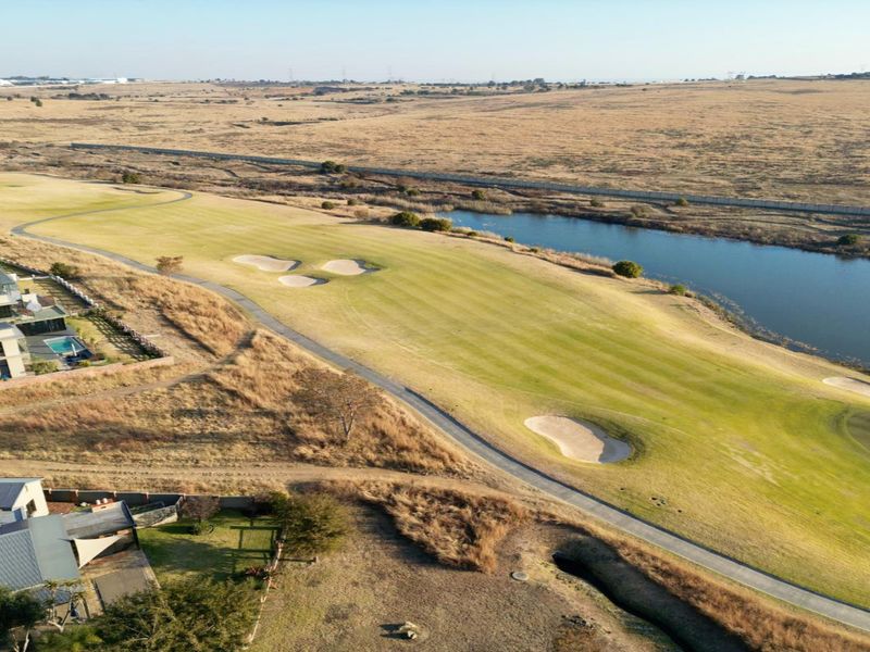 Aerial view of a residential estate bordering a golf course and a large water feature, showcasing the surrounding landscape and property positioning.