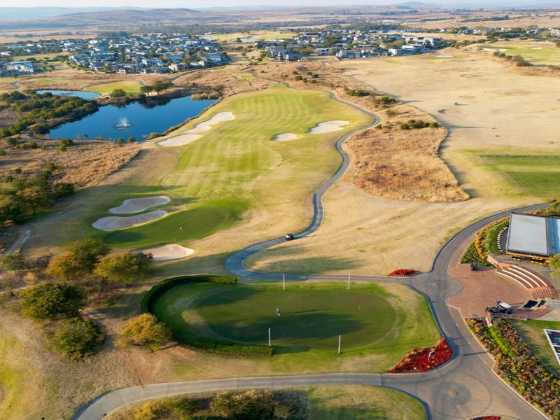 An expansive aerial view of a residential golf estate featuring manicured greens, water hazards, paved pathways, and the clubhouse facility.