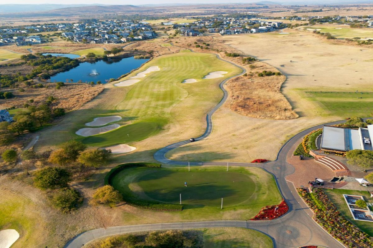 An expansive aerial view of a residential golf estate featuring manicured greens, water hazards, paved pathways, and the clubhouse facility.