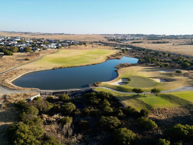 An aerial view of a residential golf estate featuring a large lake, manicured greens, and surrounding natural landscape.