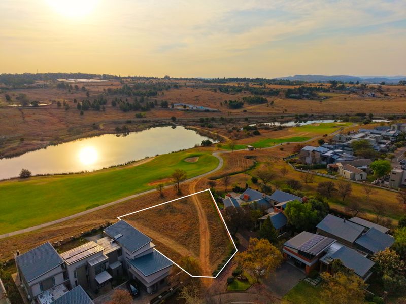 Aerial view of a vacant residential plot highlighted with boundary lines, situated in a scenic estate near a lake and golf course.