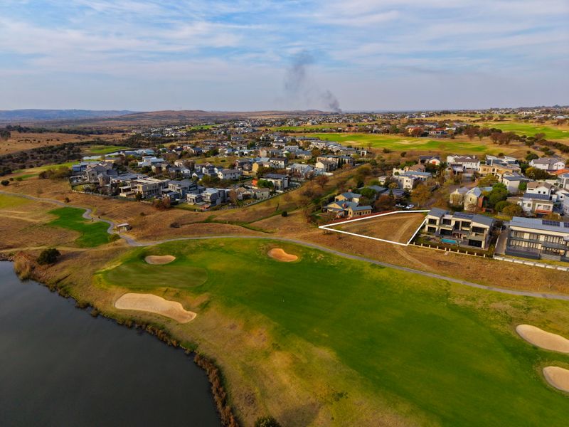 Aerial view of a vacant residential plot situated within a golf estate, featuring proximity to the golf course and a lake.