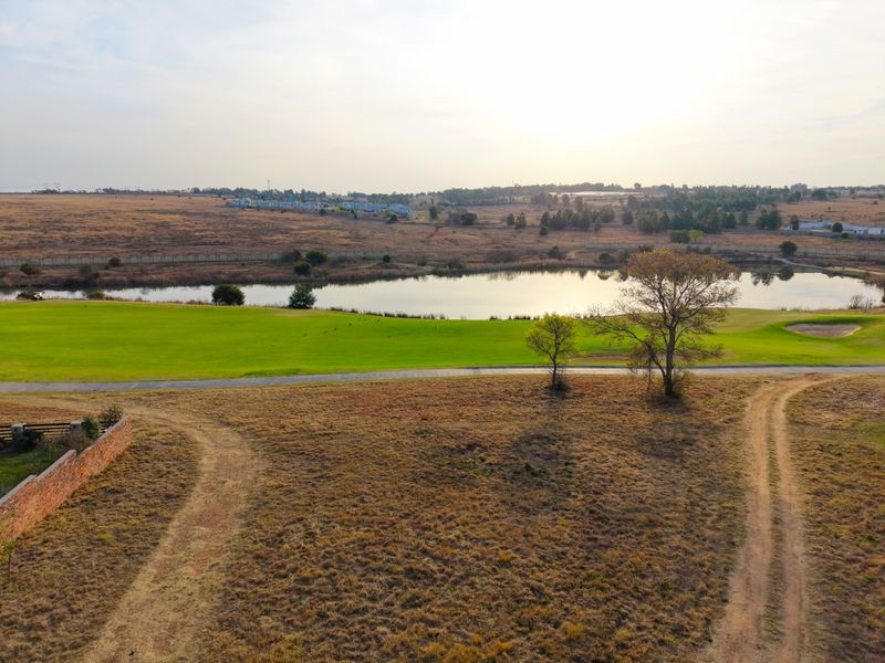 Aerial view of a vacant residential plot overlooking a golf course and a scenic lake, showcasing the natural landscape and surrounding estate.