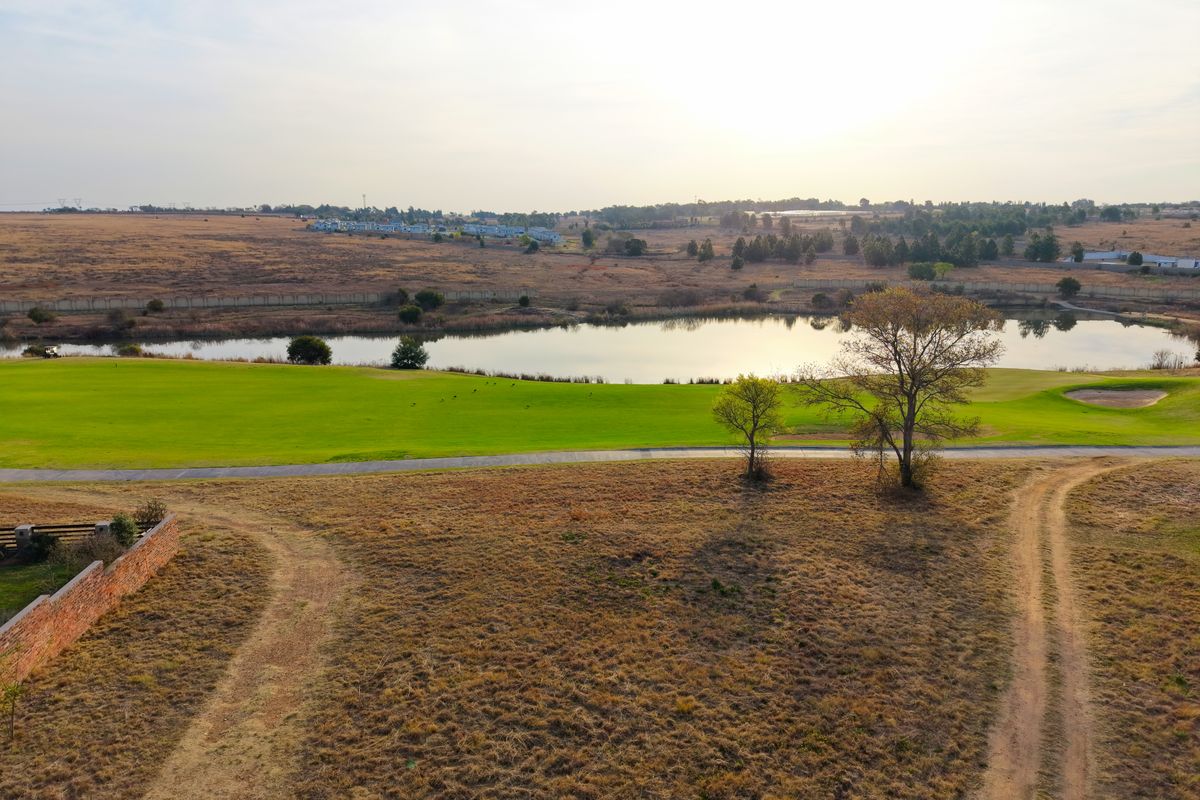 Aerial view of a vacant residential plot overlooking a golf course and a scenic lake, showcasing the natural landscape and surrounding estate.