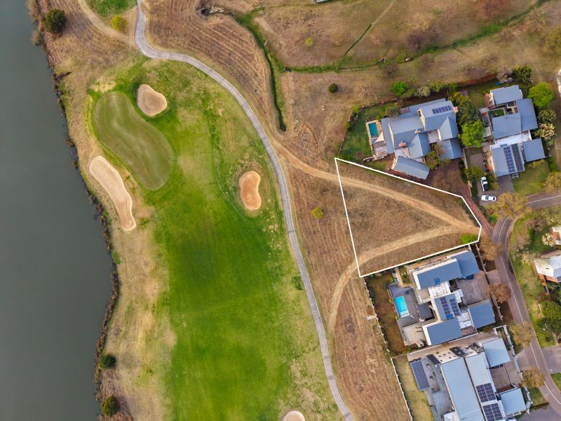 Aerial view of a vacant residential land plot situated adjacent to a golf course and water feature, offering prime development potential.