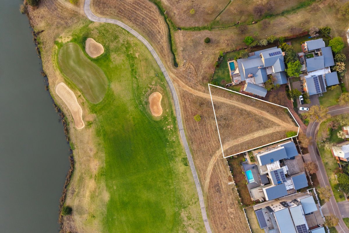 Aerial view of a vacant residential land plot situated adjacent to a golf course and water feature, offering prime development potential.