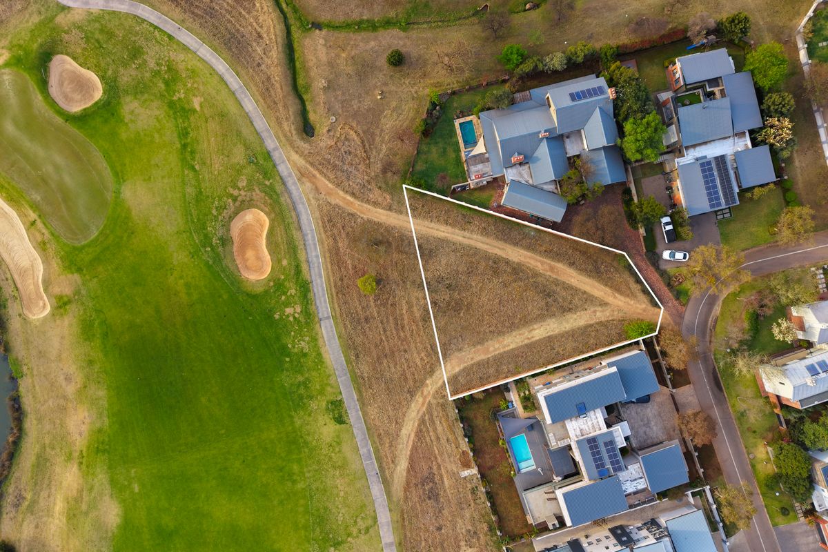 Aerial view of a vacant residential land plot situated adjacent to a golf course, offering a prime location for development.