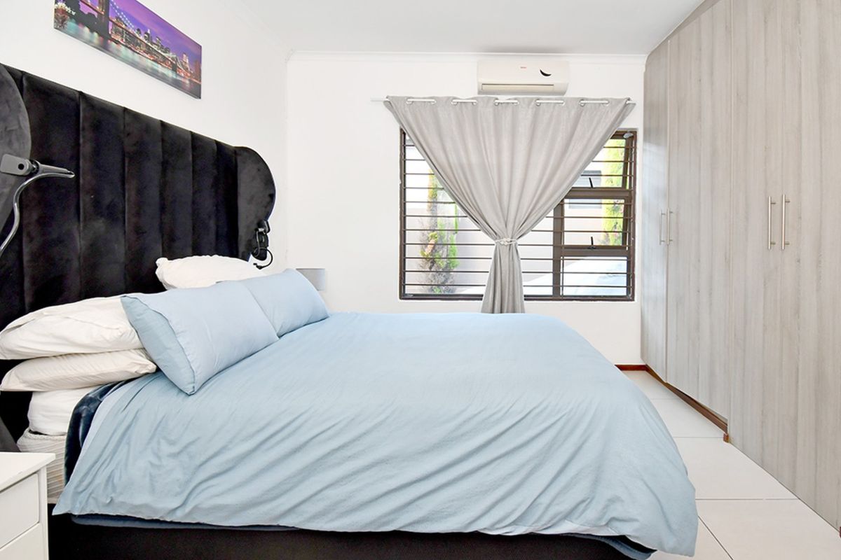 A well-maintained bedroom featuring built-in wardrobes, tiled flooring, and a wall-mounted air conditioning unit.