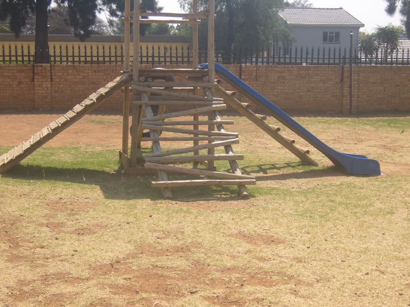 Outdoor communal garden area featuring a brick perimeter wall with security spikes and a weathered wooden playground structure with a slide.