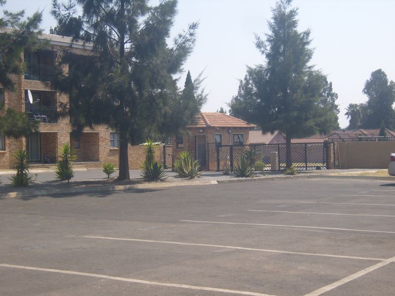 Exterior view of the apartment complex featuring a paved parking area, security guard house, and established landscaping.