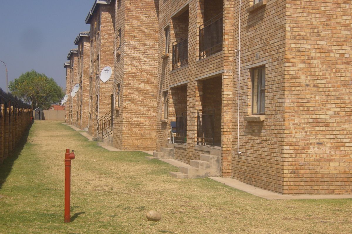 Exterior view of a multi-story apartment complex featuring face brick construction, private balconies with metal railings, and communal lawn space.