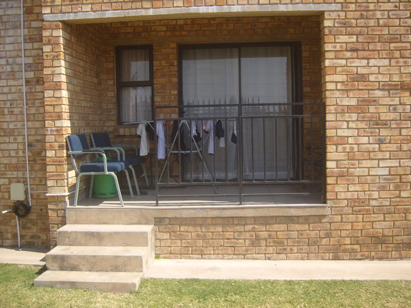 A ground-level patio featuring face brick construction, a sliding glass door entrance, and a metal safety balustrade.