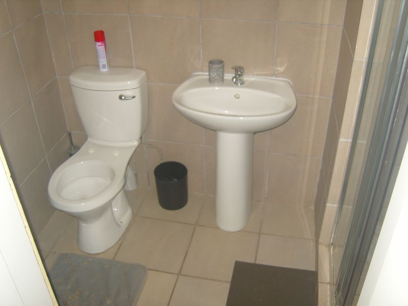A functional bathroom featuring a pedestal basin, toilet, and tiled finishes, providing a clean and practical space.