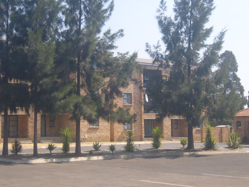 A view of a multi-story face brick apartment complex featuring paved driveway access and established garden landscaping.