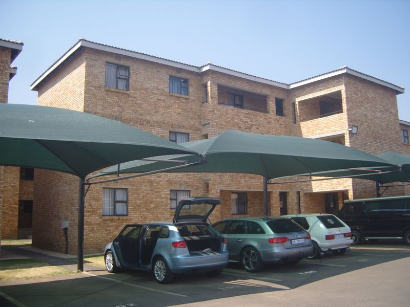 Exterior view of a multi-story face brick apartment complex featuring covered parking bays and private balconies.