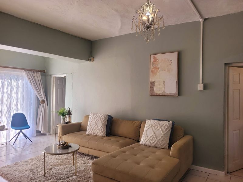 A living room featuring tiled floors and a chandelier, with visible wall and ceiling imperfections requiring cosmetic attention.