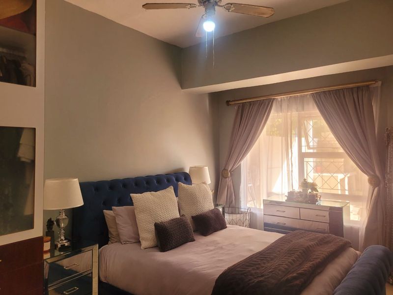 A cozy bedroom featuring a ceiling fan, built-in storage, and a window with security bars, providing a comfortable and functional living space.
