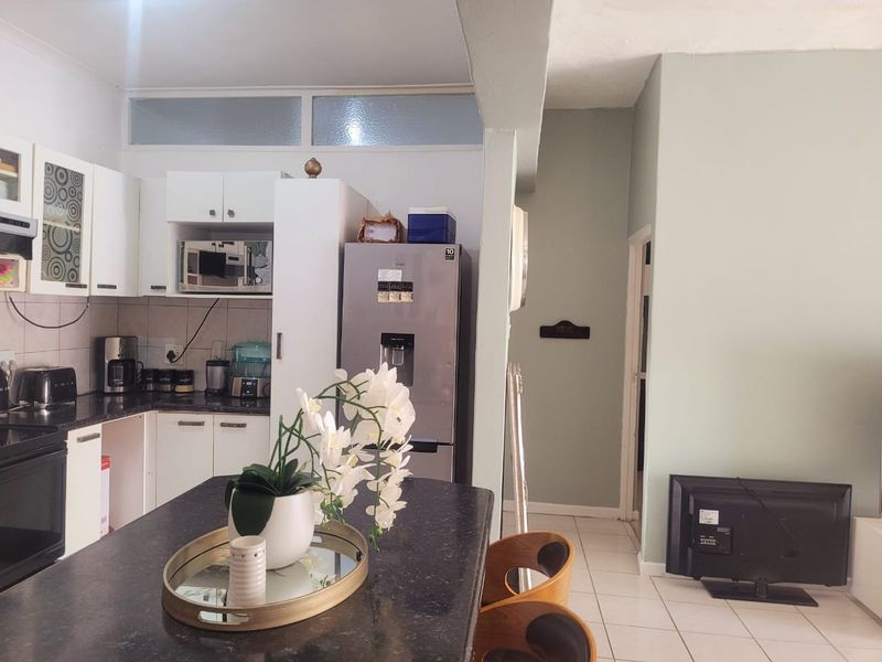 Open-plan kitchen and living area featuring white cabinetry, dark granite countertops, and neutral tiled flooring, creating a functional and connected living space.