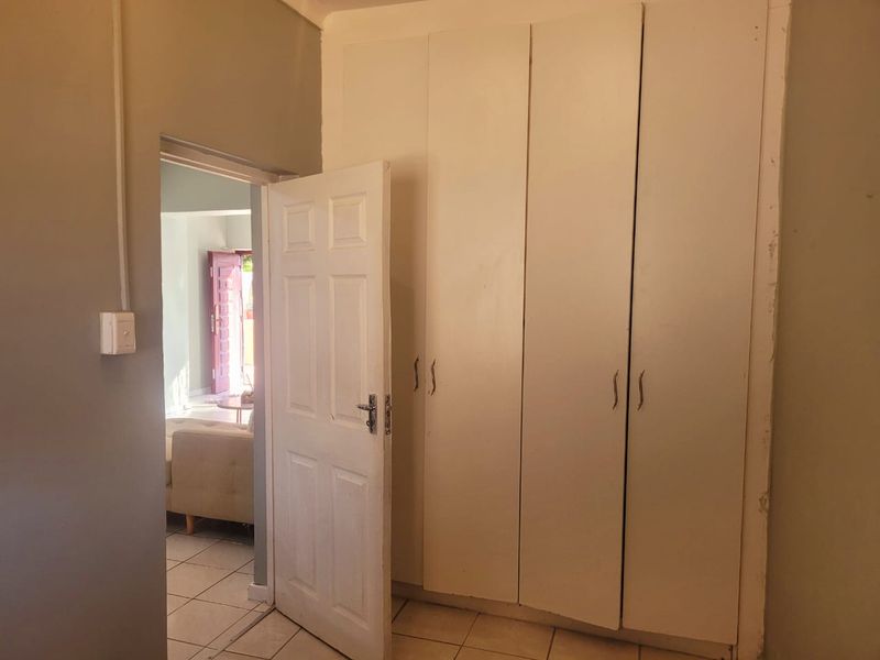 A bedroom featuring built-in cupboards and tiled flooring, with a view through the doorway into the adjacent living area.